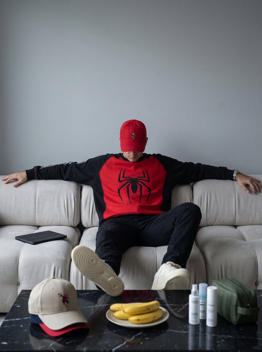 Hombre con buzo Spider-Man rojo y negro y gorra roja sentado en un sofá