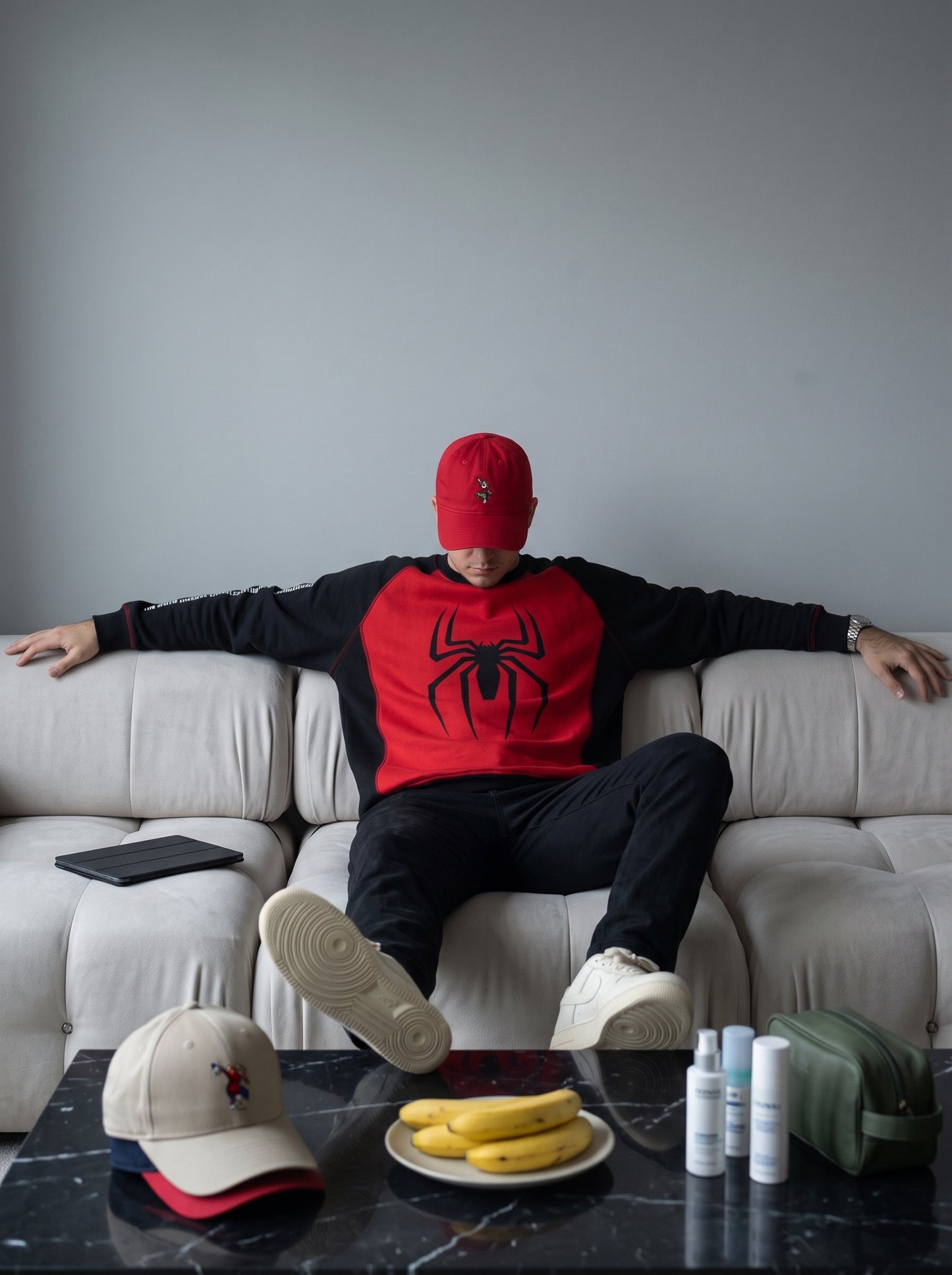 Hombre con buzo Spider-Man rojo y negro y gorra roja sentado en un sofá